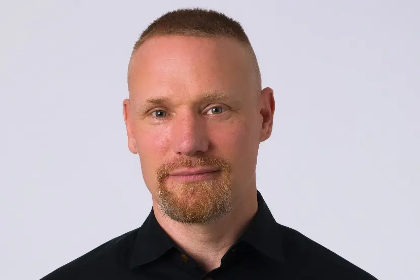 A man wearing a back shirt, smiling at the camera.