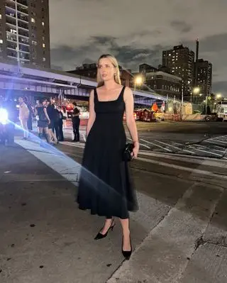 Who What Wear editor Kristen Nichols poses in New York City at night wearings a black fit and flare dress, mini clutch bag, and pointed-toe slingback pumps