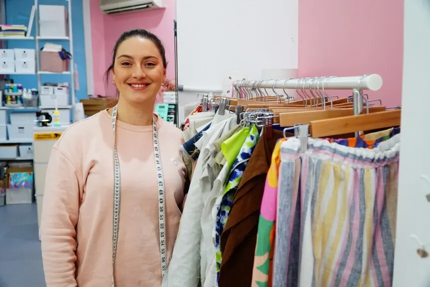 A woman stands next to a rack of fabric, smiling at the camera.