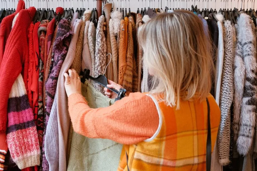 A woman looks through a number of clothes on a rack in an op shop.