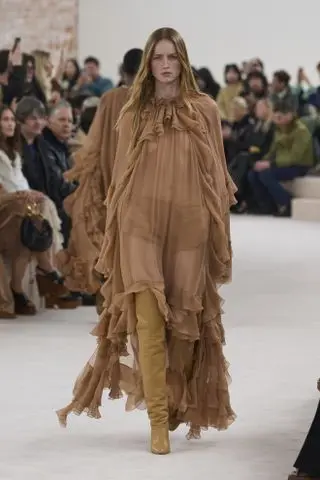 A model at the Chloé autumn/winter 2024 runway show wearing a sheer ruffled maxi dress with thigh-high boots.