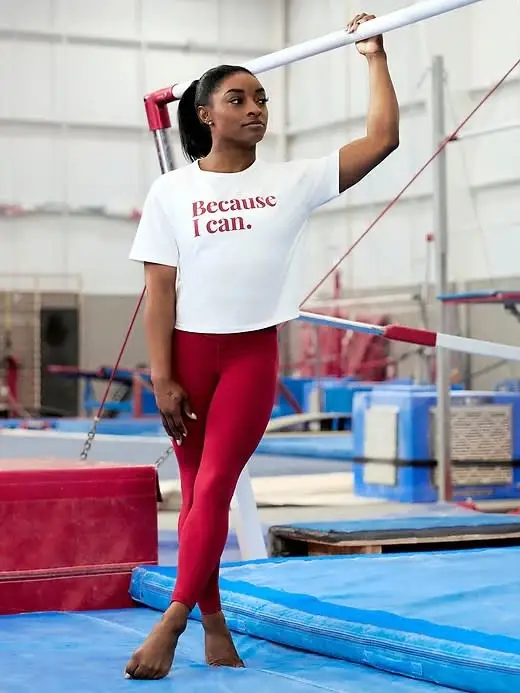 Simone Biles wears a white creative t-shirt and red athleta leggings.