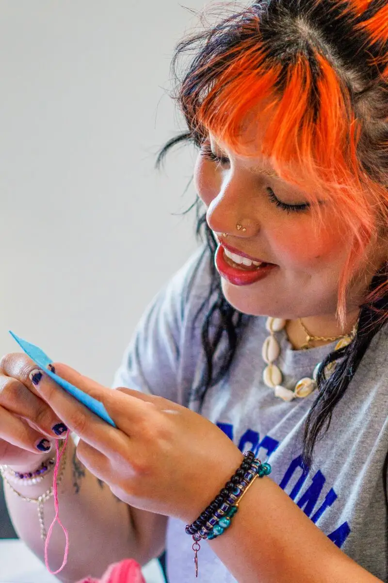 A person with orange-dyed bangs works on a sewing design at the Radical Sewing Club.