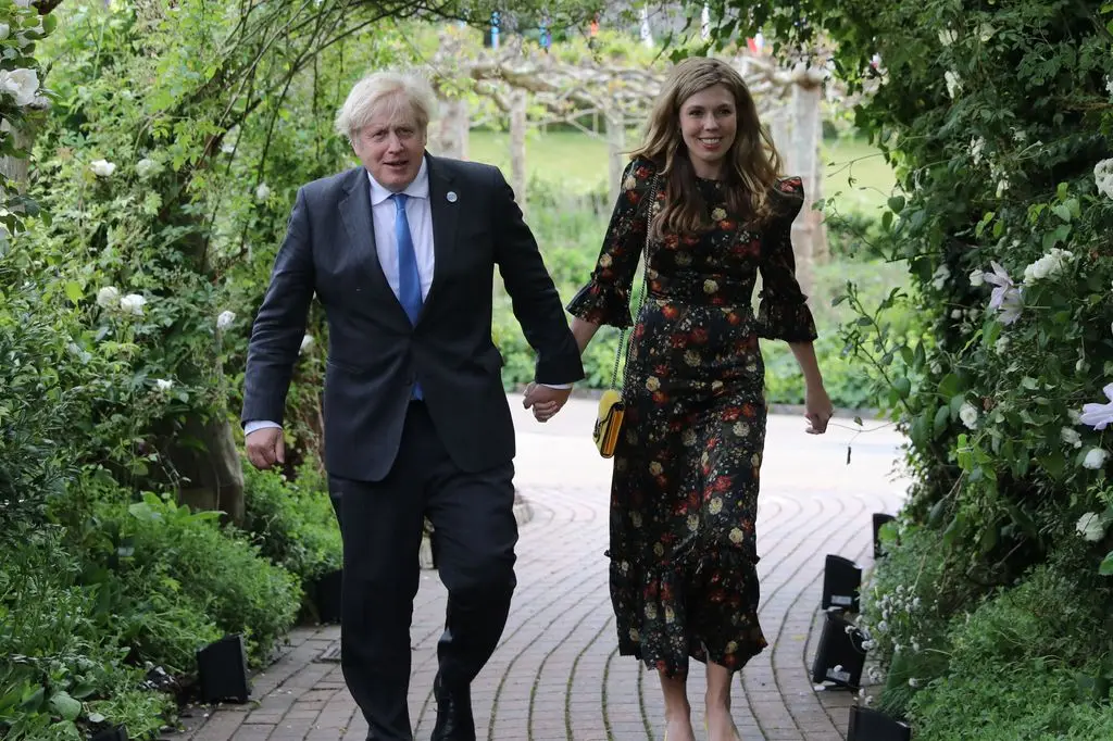 Boris Johnson and his wife Carrie Johnson walking through a floral arch in a garden