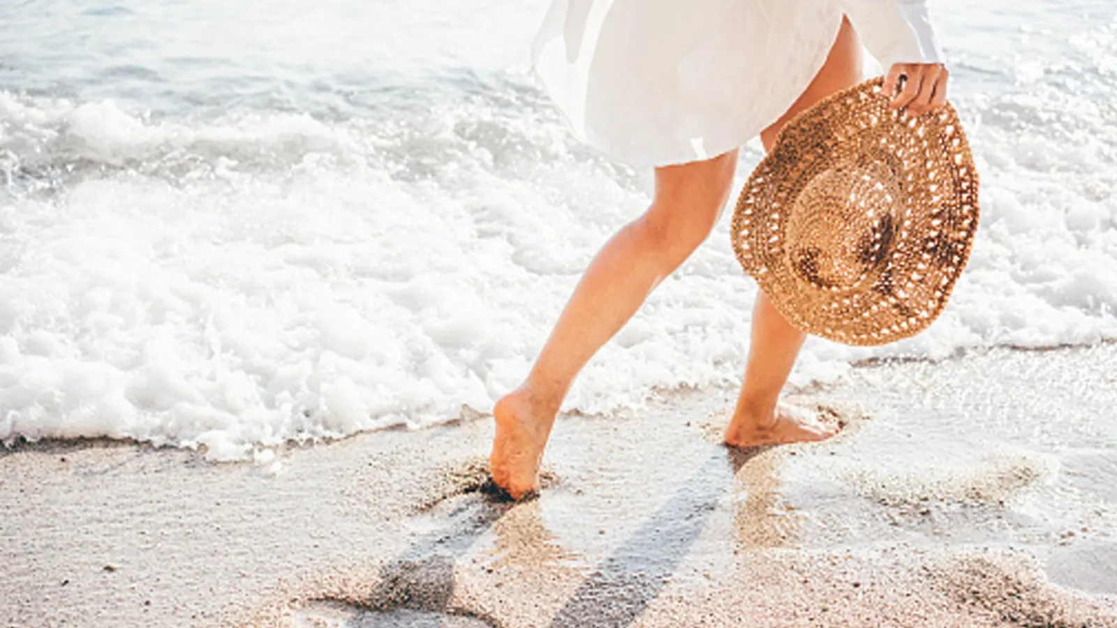 woman wearing white dress on the beach holding hat