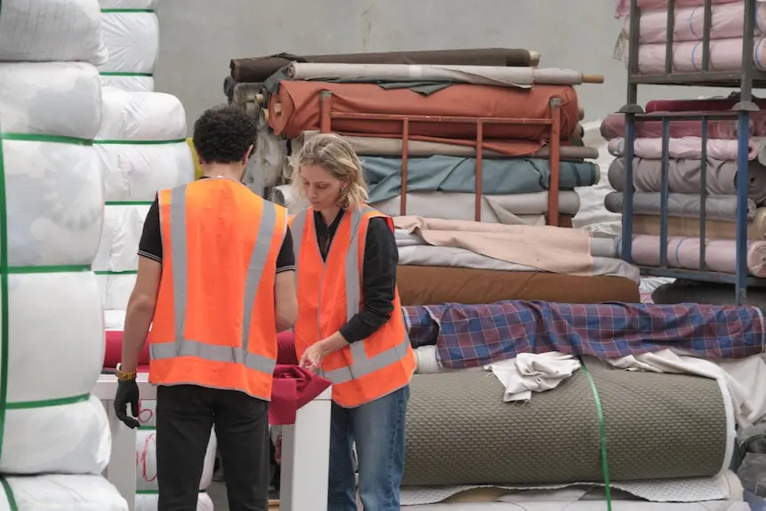 A woman in a hi-vis vest inspects fabric at a factory.