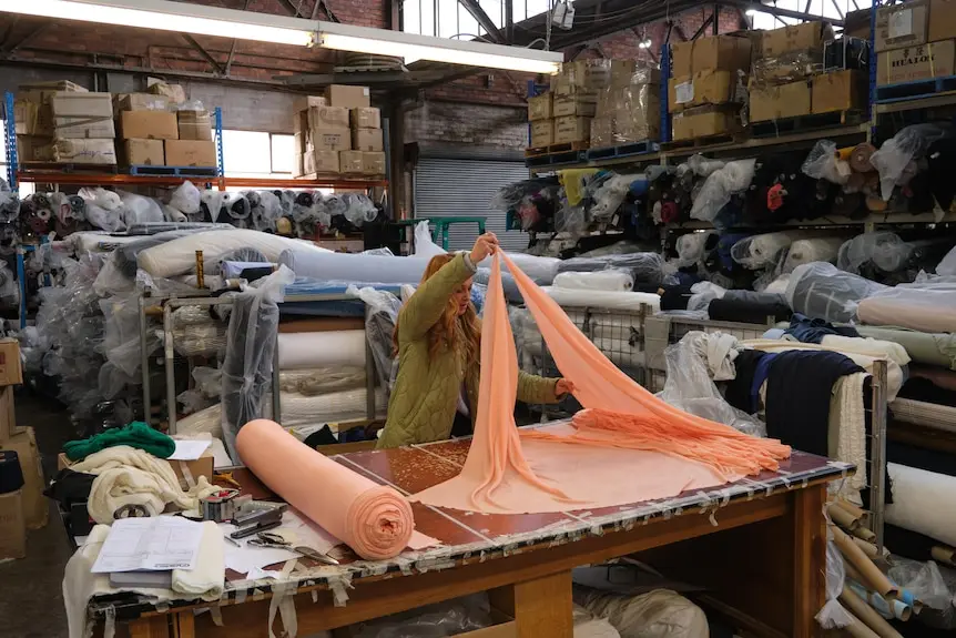 Woman cutting fabric on table inside warehouse full of fabric