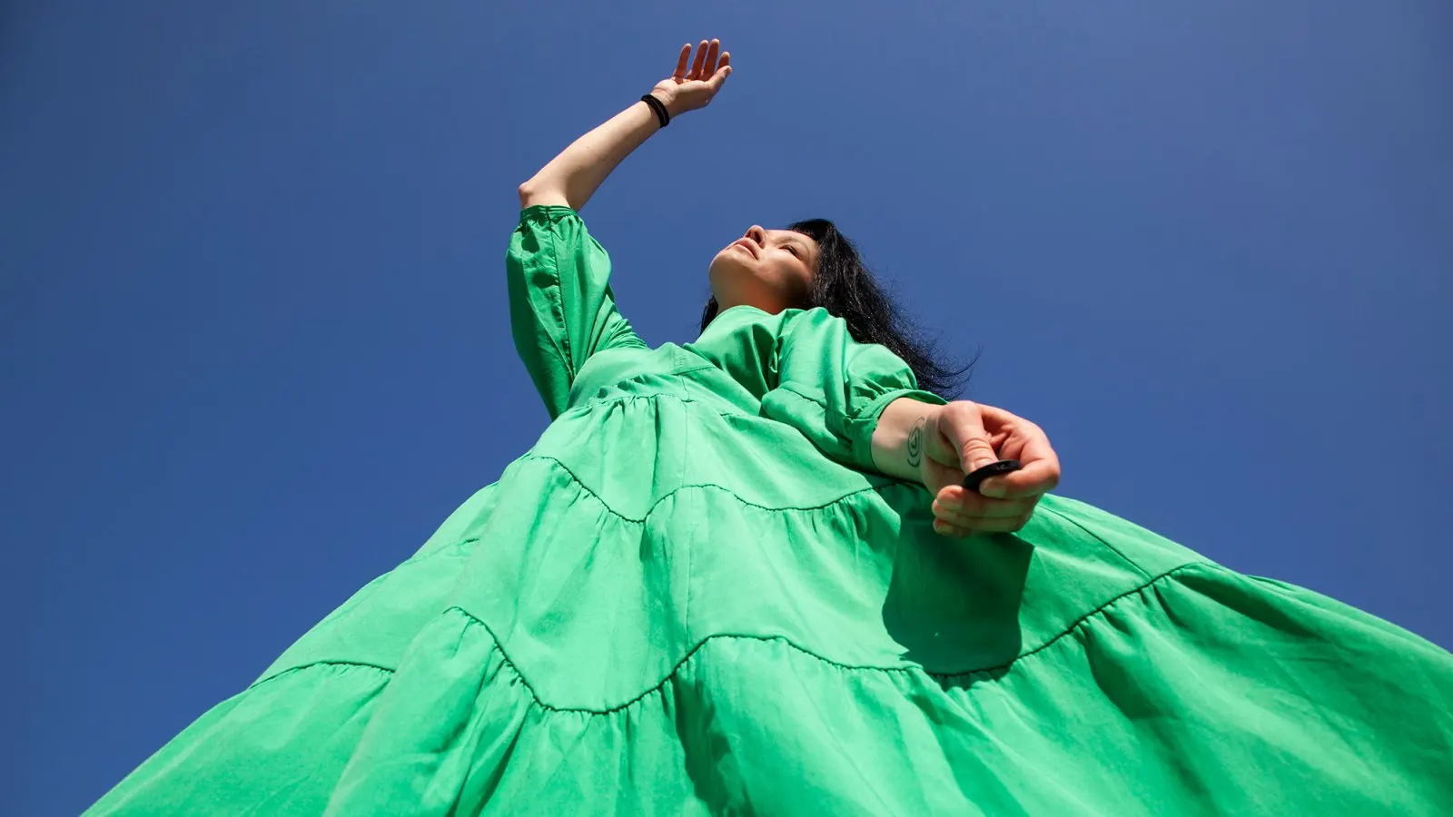 Low angle view of woman in green dress standing against clear blue sky