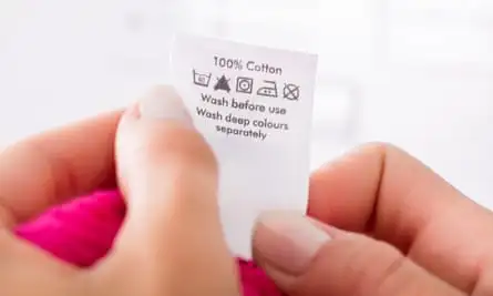 A woman’s hands holding up a clothing care label that says the garment is 100% cotton