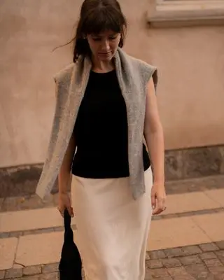 senior fashion editor Halie LeSavage wears a black shirt with a white column skirt and gray sweater over her shoulders to the Rotate show at Copenhagen Fashion Week