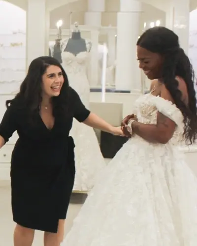 A person in a black dress reacts happily to a person in a white wedding dress