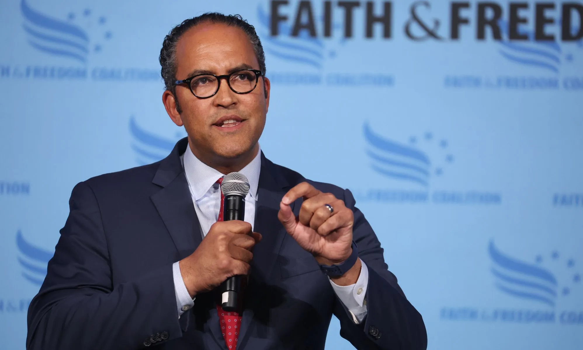 Will Hurd, who is a 2024 Republican presidential candidate, wears a light shirt, red tie and dark blue jacket as he speaks at a rally