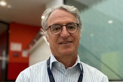 A man wearing a striped shirt, glasses and a lanyard smiles into the camera.