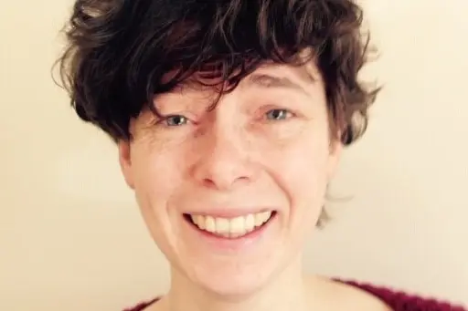 A woman with short, curly brown hair smiles into the camera.