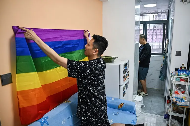 Willy (left) from Taiwan and Louis, from mainland China, in their apartment in Shenzhen, Guangdong, December 16, 2023. Willy hangs the rainbow flag, a symbol of the LGBTQ community, behind their sofa. (Hector Retamal/AFP)