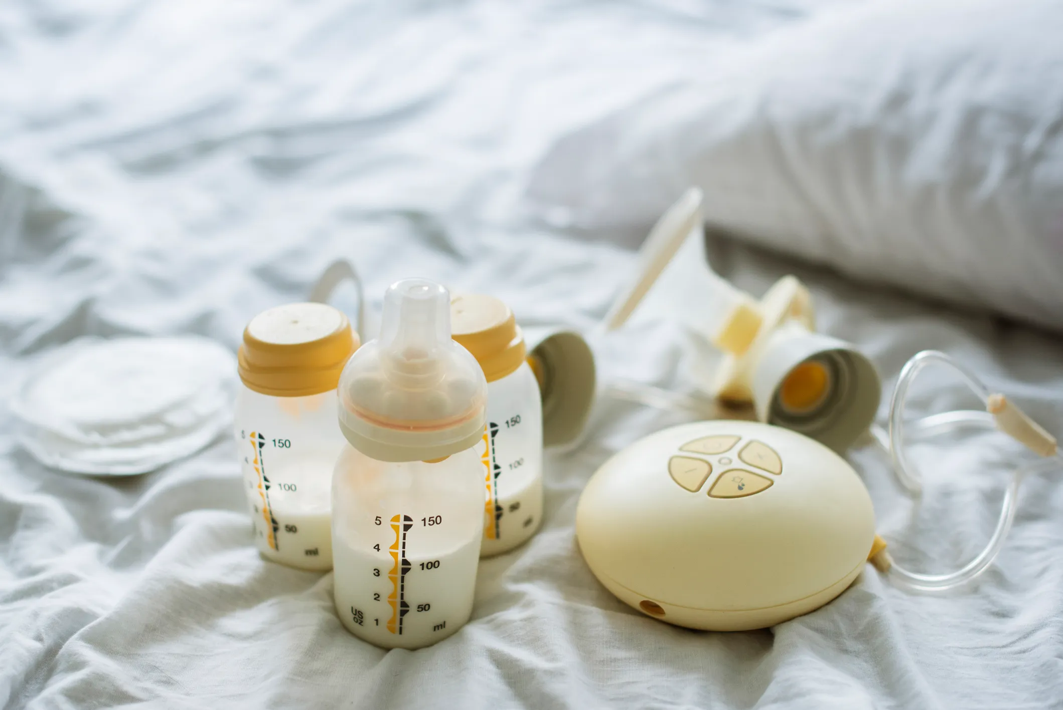 Some of the equipment used by people who breastfeed or chestfeed their children. An electric breast pump is pictured alongside three bottles on a bed.