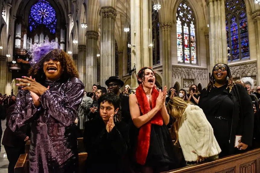 People standing and clapping, some singing, during a mass inside a church