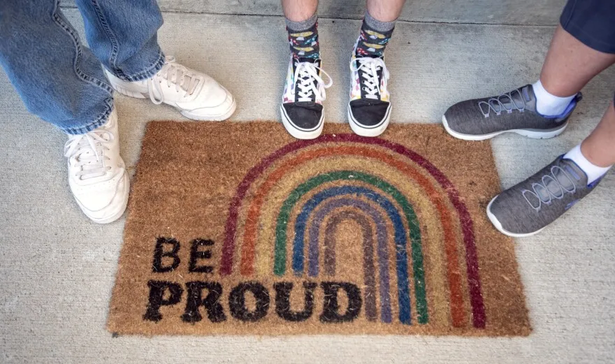 A Missouri family stands by their doormat at a home they are soon to leave — drawn out by bills that would limit the freedoms of their transgender son.