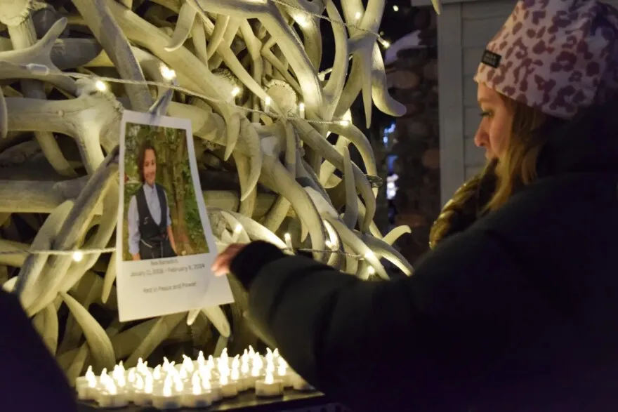 Holding a glove in her mouth, Cheyenne Syvertson hangs a photo of Nex Benedict, the nonbinary teenager who died recently in Oklahoma. She says one goal of the vigil is to make sure local gender diverse kids know they are supported.