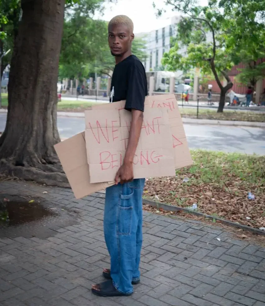 Prince Frimpong, an LGBTQ+ activist in Ghana, looks towards the camera while holding several signs in their arms