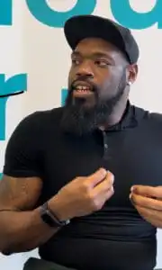 Chris Sutton (he/him), a black man wearing a back hat with a brown beard sits talking to GLAAD about LGBT Detroit, using his hands while he speaks.