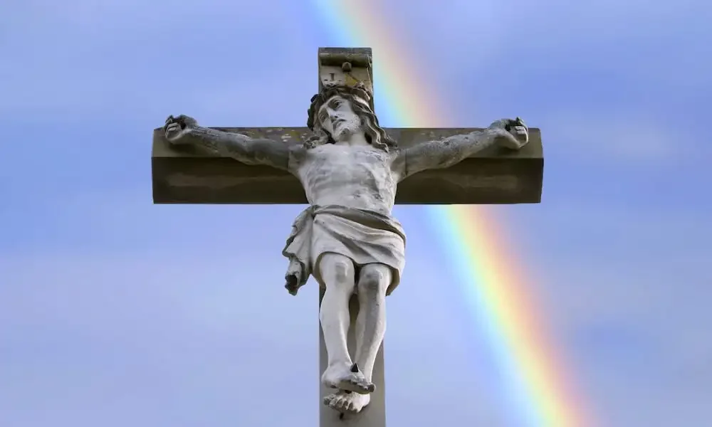 statue of Jesus on a crucifix in front of a rainbow