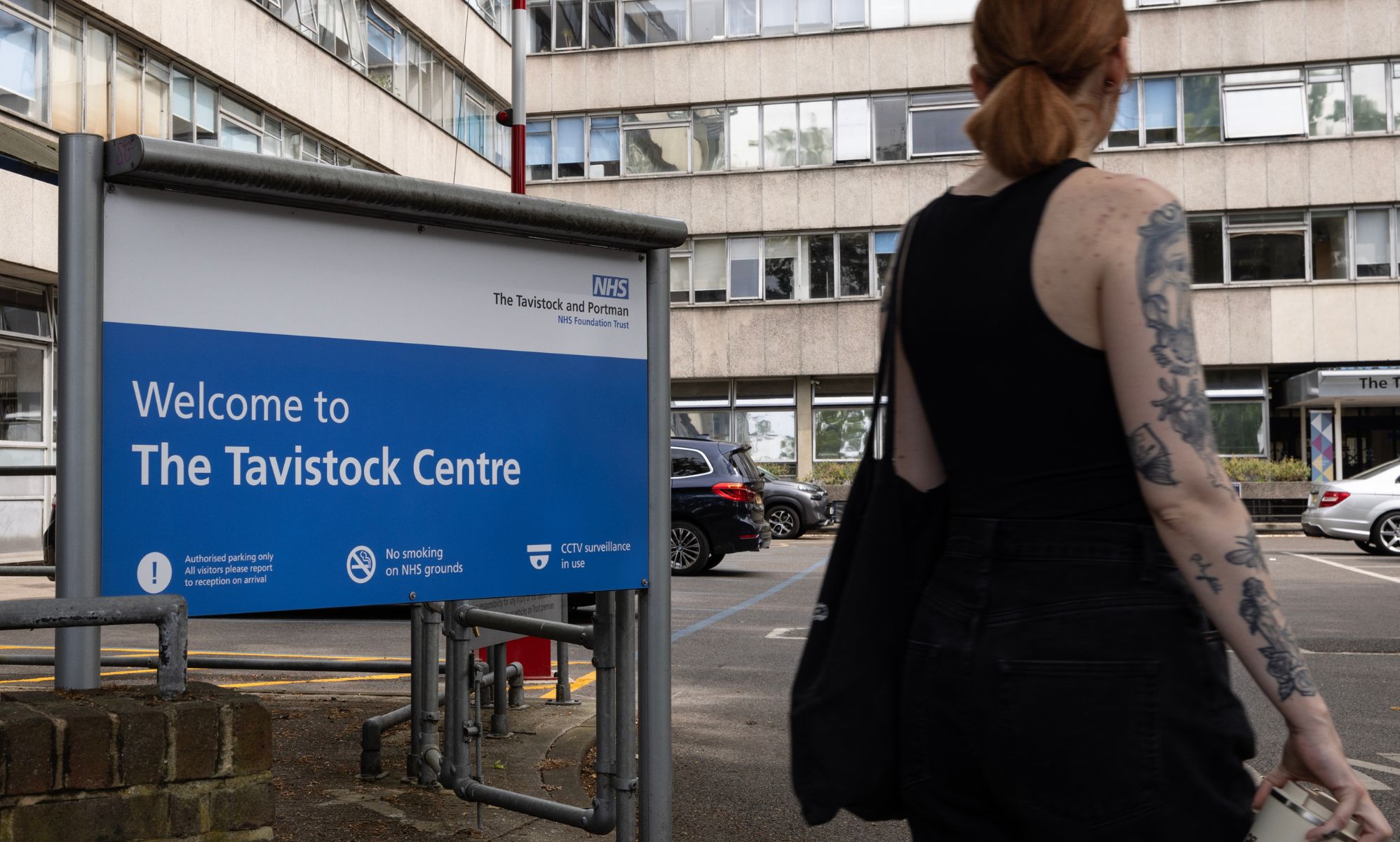 A person in a tank top stands outside infront of the Tavistock Centre sign.