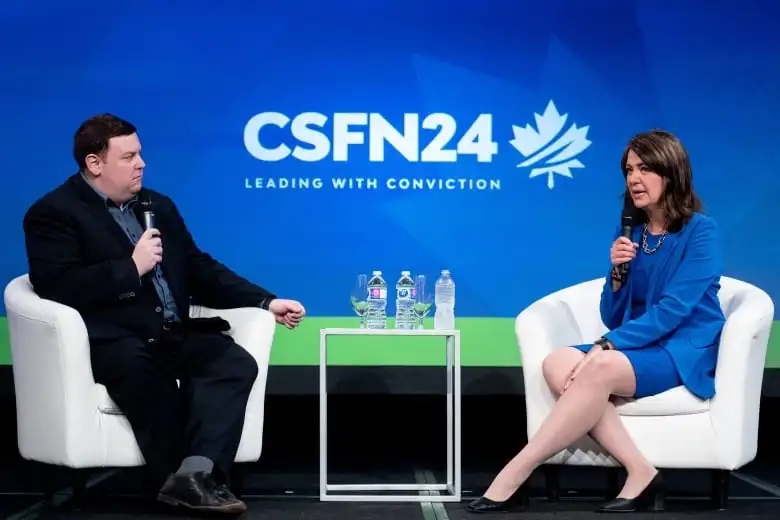 two people sit in chairs on a stage, talking into microphones.