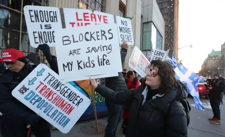 A person holds up a sign saying 'blockers are saving my kids life' as part of a protest in Ottawa.