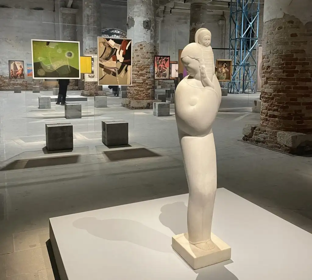 A white marble sculpture erected in an exhibition hall, which also has a lot of paintings hung on glass panels.