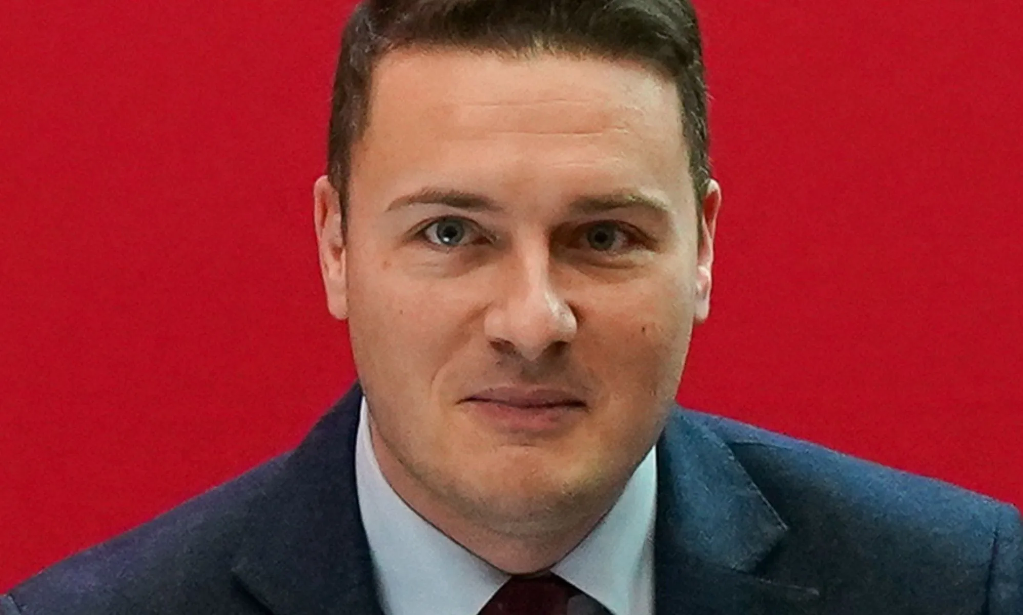 Wes Streeting at a Labour conference in front of a red background.