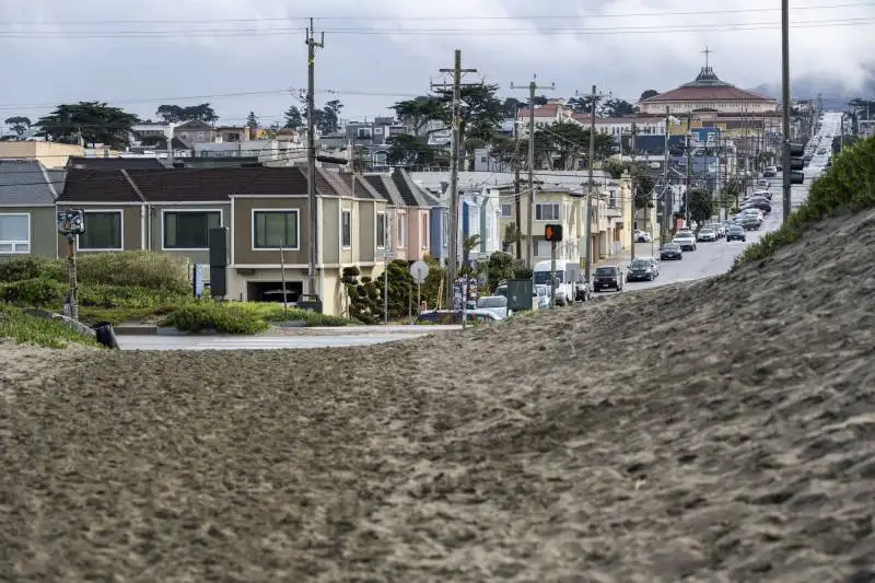 A view of a residential neighborhood with a sandy coastline on the other side of a road.