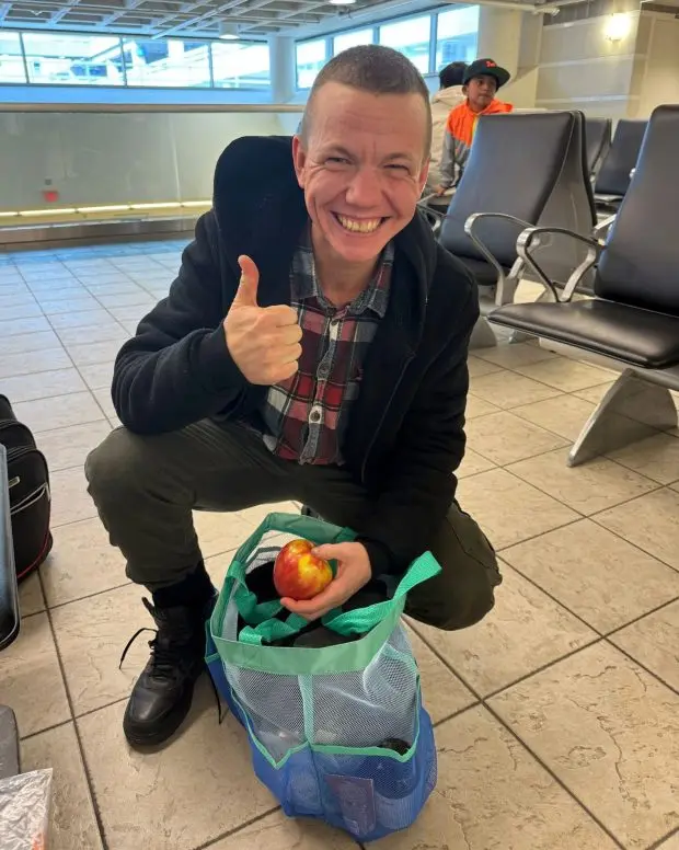 A man crouches over a small bag and gives a thumbs up.