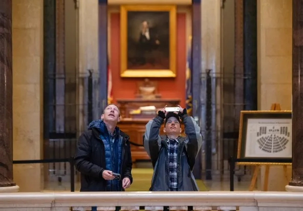 Two people look up, one taking a photo with a cell phone.