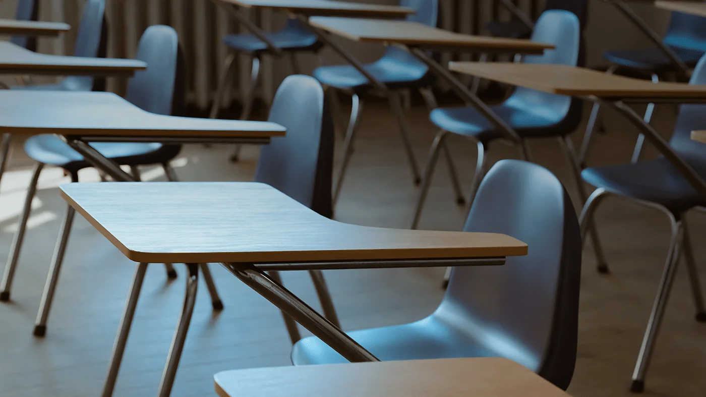 Empty desks and chairs are seen in a classroom.