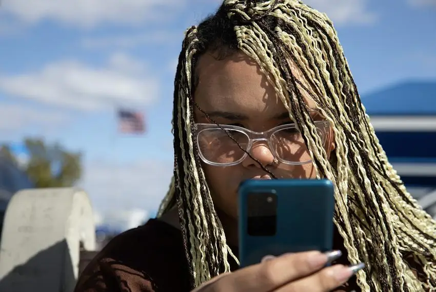 Isabella Morningstar looks at the bus route on her phone outside a car dealership on Nov. 21, 2023. Once she has a job, she will start saving to buy a car. Traveling around San Antonio using public transit can take hours longer than driving.