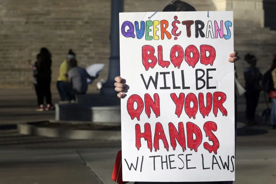 FILE - A protester outside the Kansas Statehouse holds a sign after a rally for transgender rights on the Transgender Day of Visibility, March 31, 2023, in Topeka, Kan. A new rule from President Joe Biden's administration assuring transgender students be allowed to use the school bathrooms that align with their gender identity could conflict with laws in Republican-controlled states that seek to make sure they can't. (AP Photo/John Hanna, File)