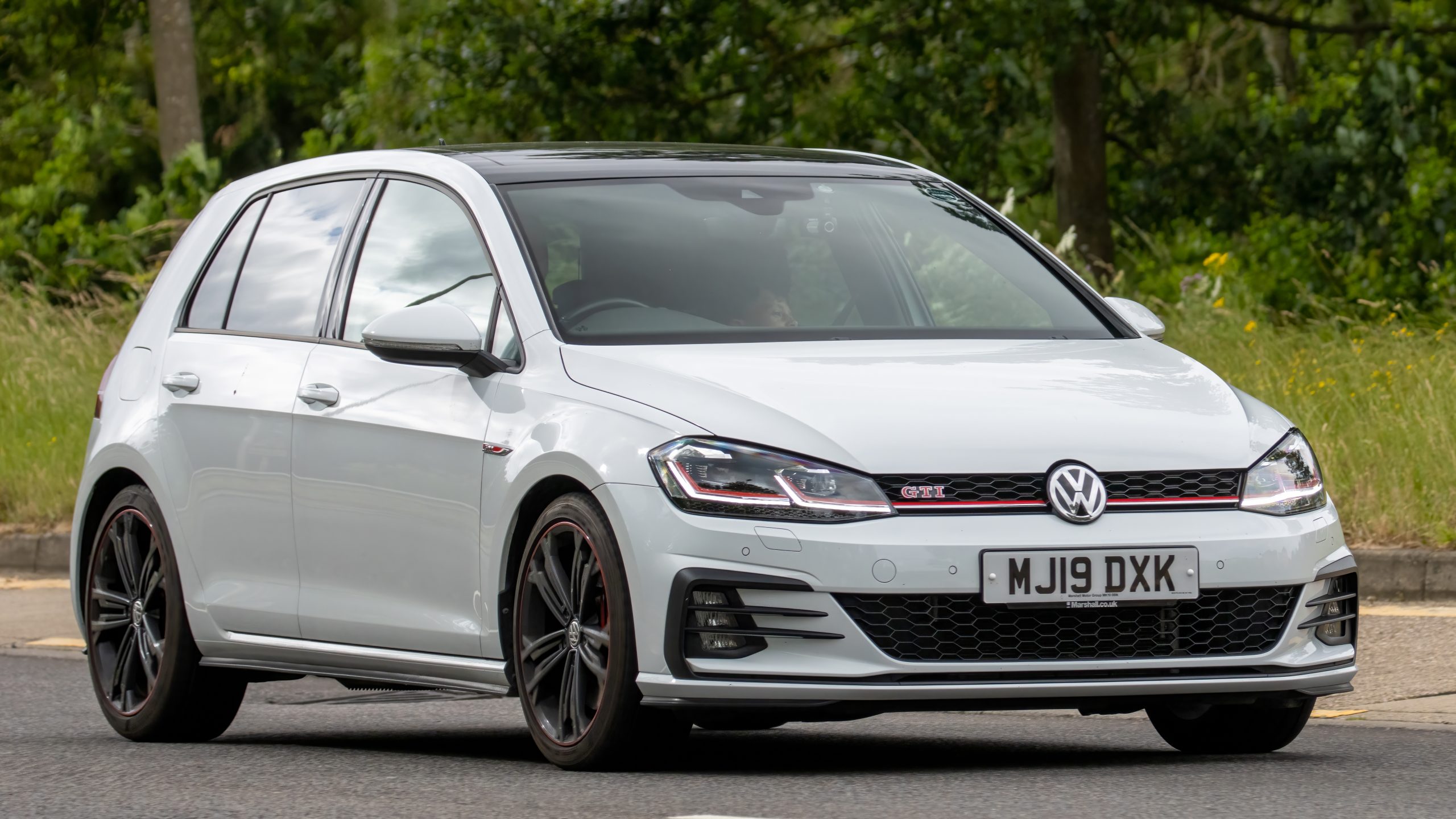 A 2019 white Volkswagen Golf GTI Performance TSI car travels along an English road