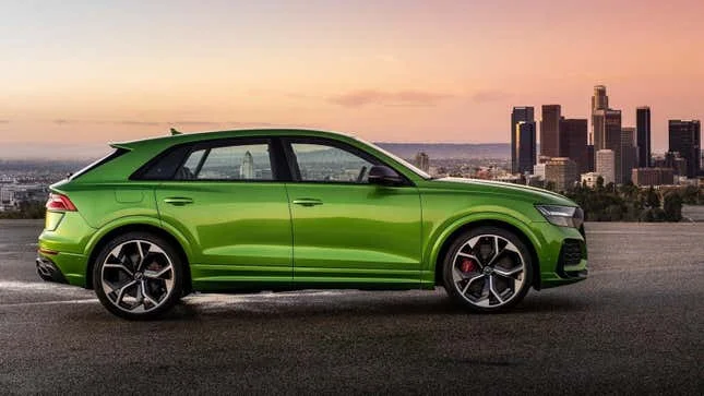 A bright green Audi RS Q8 from the side parked in front of the Los Angeles skyline at dusk