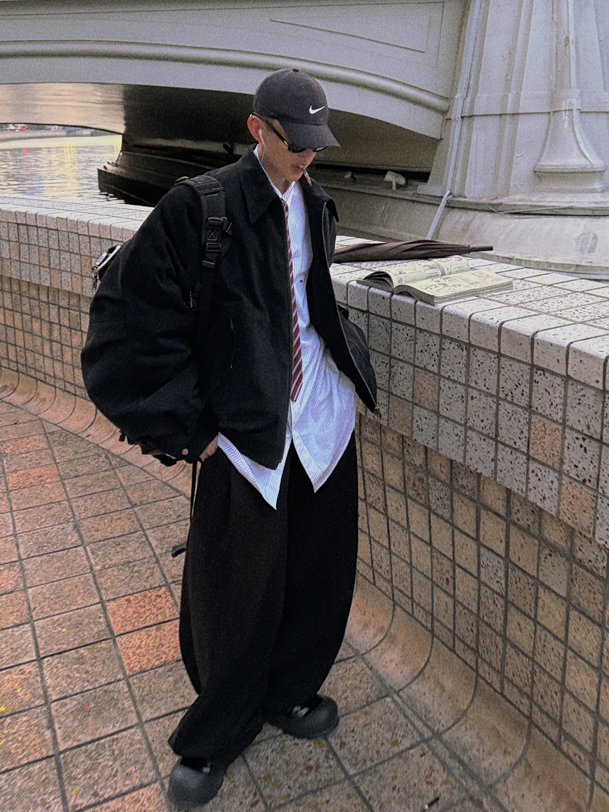 korean men's fashion: Black Oversized Coat + Loose White Button-up with Tie + Black Wide-Leg Pants + Black Cap + Nike Backpack + Chunky Shoes