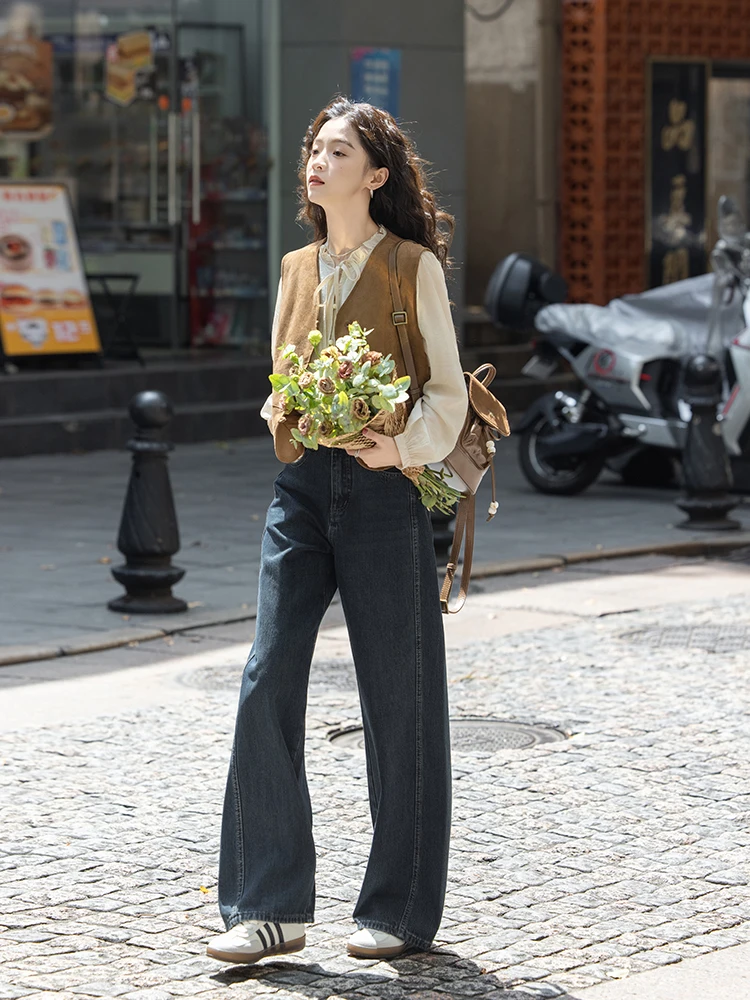 Ivory Tie-Neck Blouse + Suede Tan Vest + Dark Wide-Leg Jeans + Mini Brown Backpack + Classic White Three-Stripe Sneakers