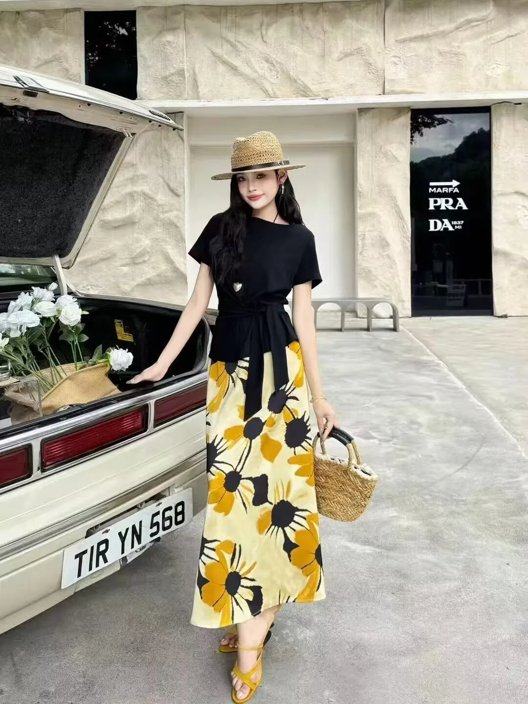 Straw Boater Hat + Black Waist-Tie Tee + Yellow-Black Floral Maxi Skirt + Wicker Handbag + Mustard Crisscross Heeled Sandals