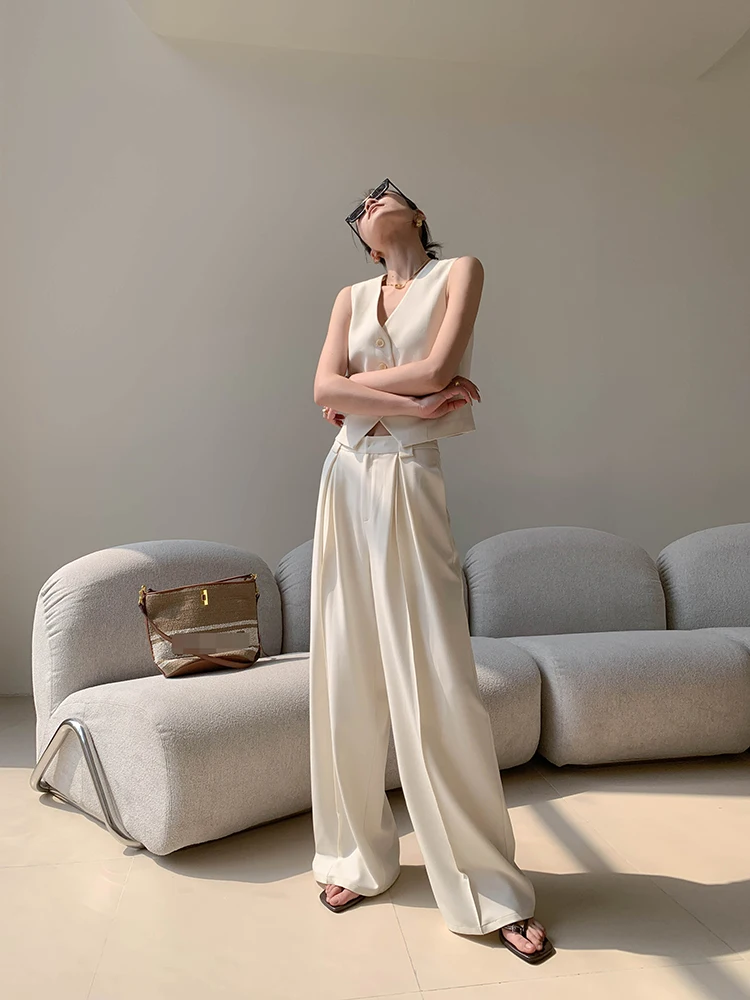Oversized square sunglasses + cream sleeveless vest + pleated cream trousers + metallic clutch