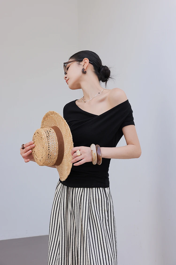 Side bun + black off-shoulder tee + straw boater hat (handheld) + vertical-stripe linen midi skirt