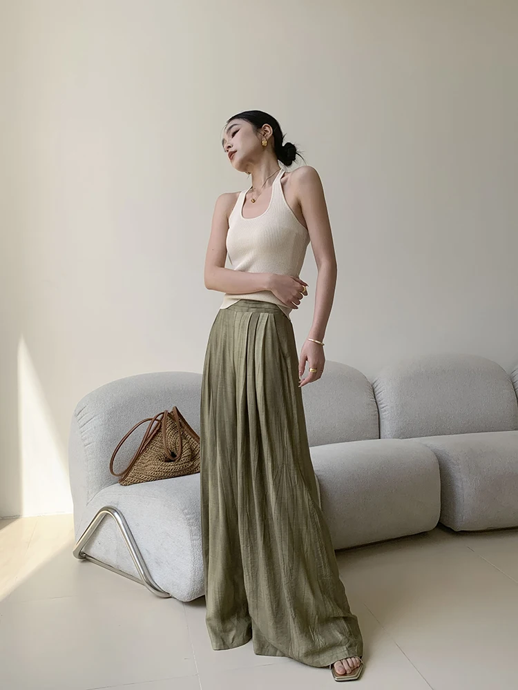 Sleek bun + ribbed halter tank + olive micro-pleat palazzo + woven pyramid bag