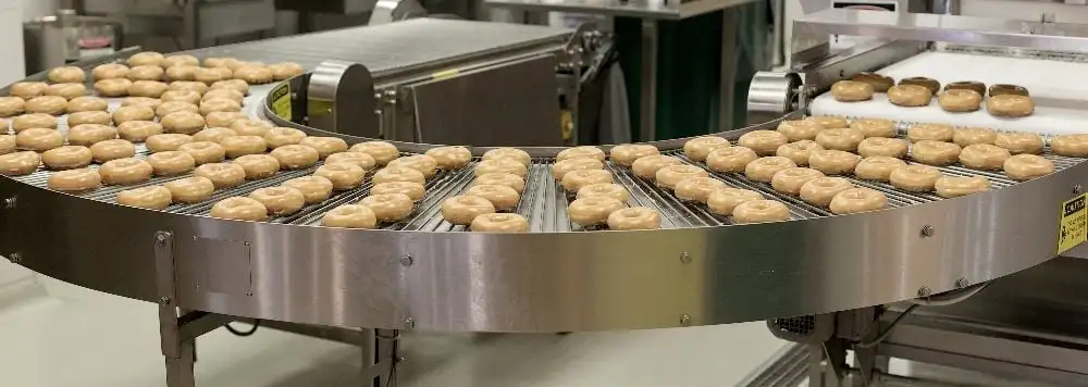 Doughnuts on a curved conveyor belt in a cafe factory in Moscow, Russia, in piece about generative AI in technology.