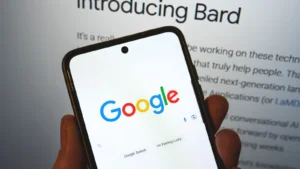 Google launches Bard AI. Google search bar on a phone in hand with release information on background. Google Bard AI vs OpenAI ChatGPT. GOOG stock and GOOGL stock.