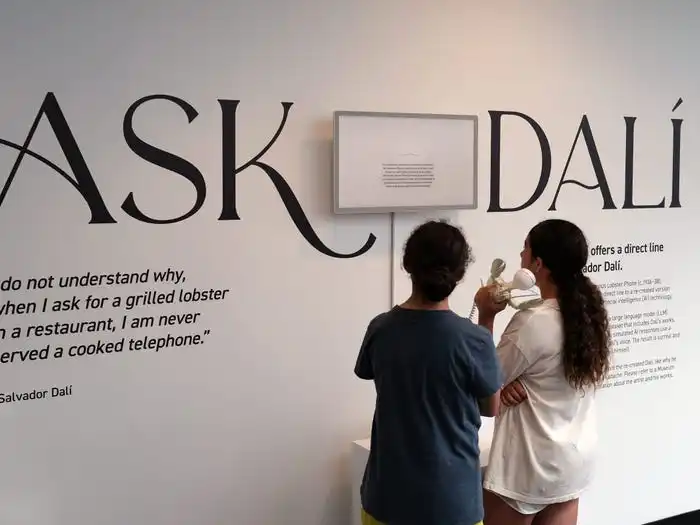 Two girls using a white phone with a lobster staring at a large white wall with the words 
